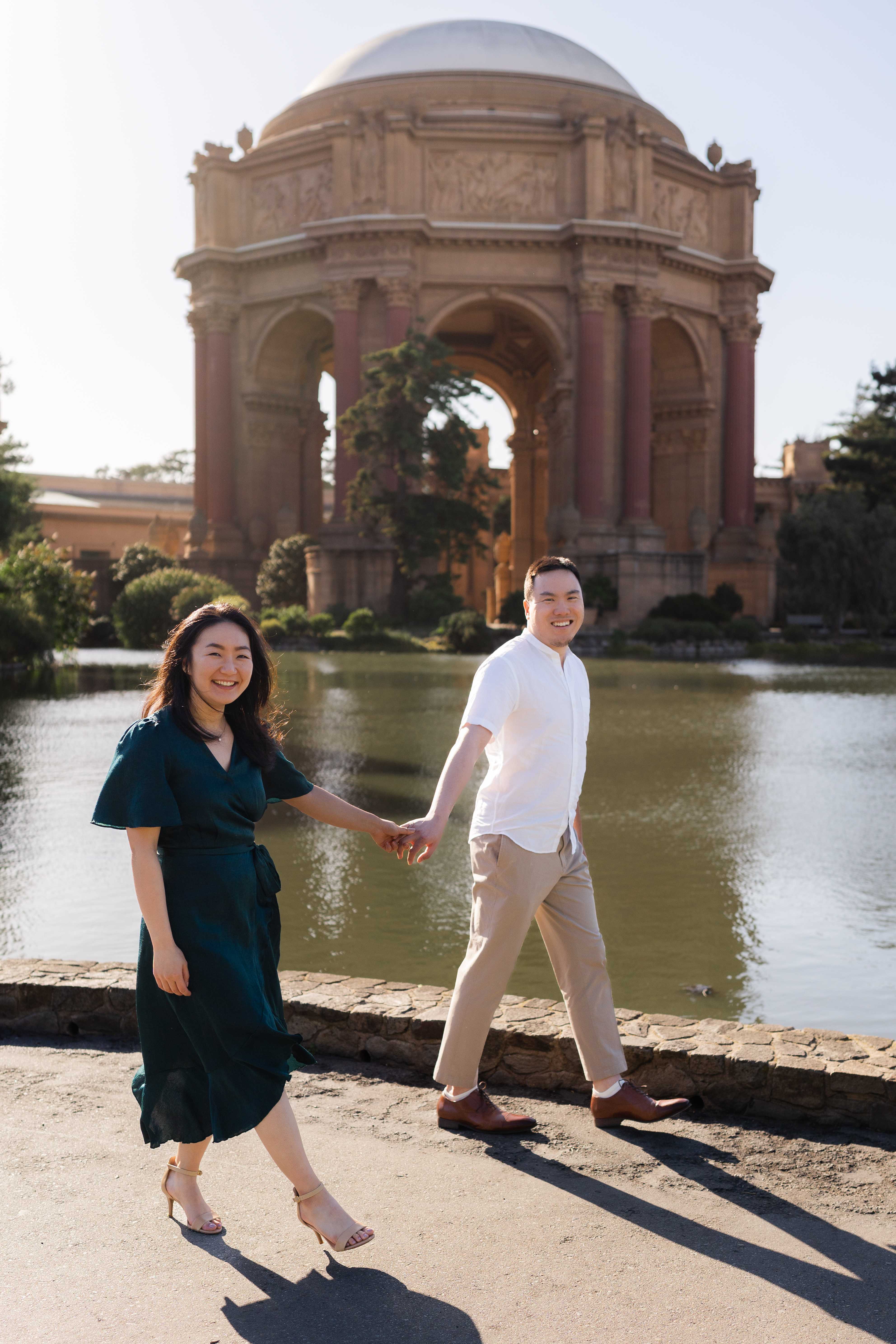 Couple walking hand in hand and laughing in front of the Palace of Fine Arts rotunda reflected in the lagoon, San Francisco